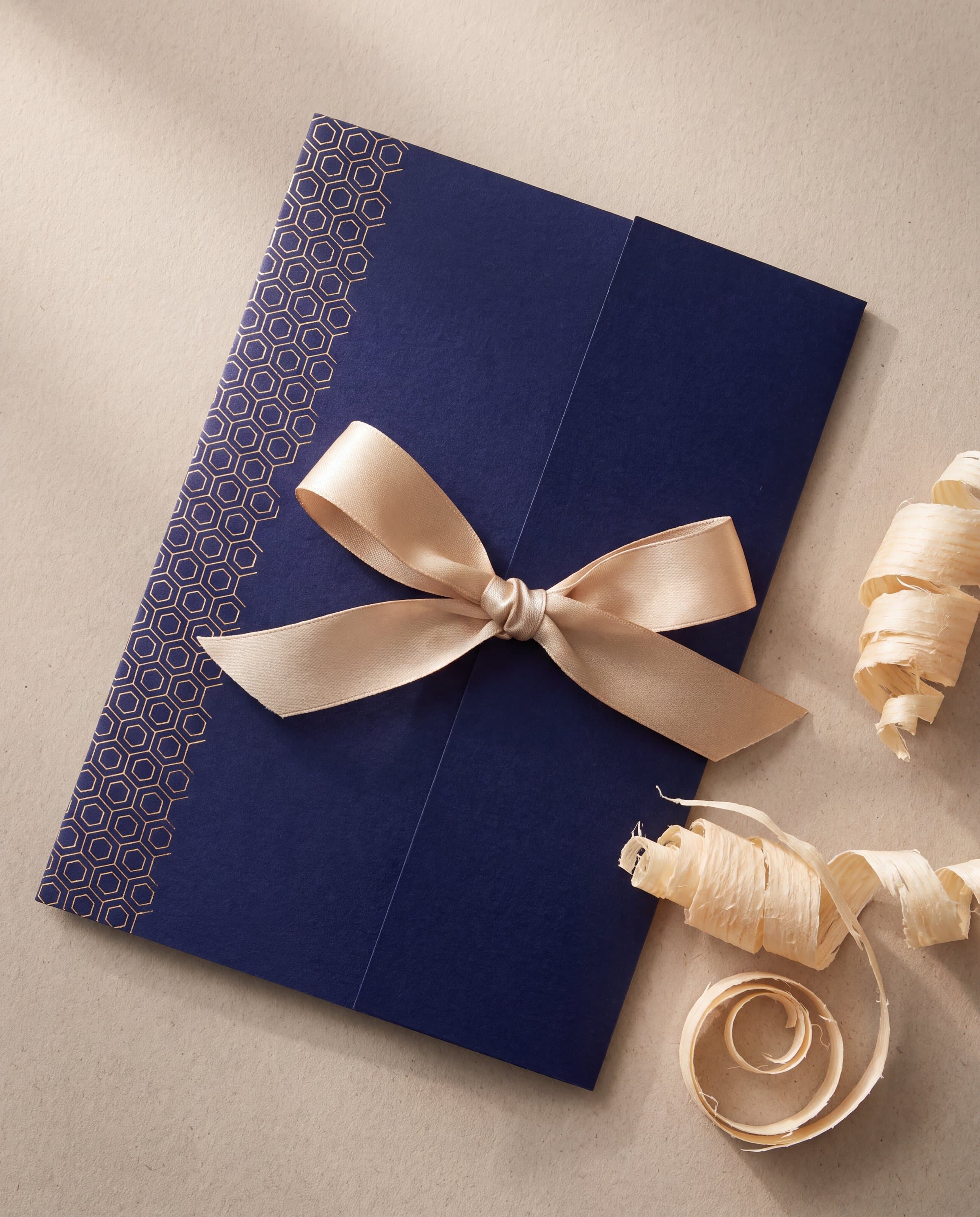 Papier bleu nuit bordé d’alvéoles dorées, noué d’un ruban champagne